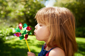 Image showing Young girl, outdoor and blowing pinwheel, garden and enjoying freedom of outside and happy. Pretty little child, backyard and summer for playing, toy and windmill for school holidays and happiness