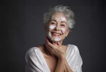 Image showing Elderly woman applies facial cream, gracefully embracing a skincare routine