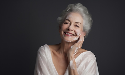 Image showing Elderly woman applies facial cream, gracefully embracing a skincare routine
