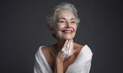 Image showing Elderly woman applies facial cream, gracefully embracing a skincare routine