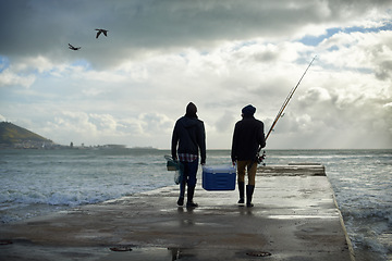 Image showing Back, walking and beach with fishermen, cooler box or activity with equipment or weekend break. People, ocean or friends with gear for hobby or rod with waves, talk or seaside with nature and cloudy