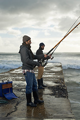 Image showing People, fishing and friends at beach on weekend, relaxing and casting a line by ocean. Men, fisherman and cloudy sky on vacation or holiday, hobby and bonding by wave and support on outdoor adventure