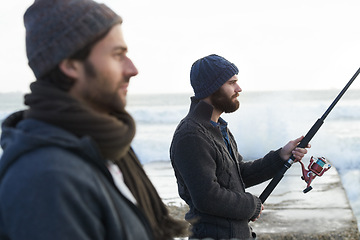 Image showing People, fishing and friends for bonding at beach, relaxing and casting a line by ocean waves. Men, fisherman and together on vacation or holiday, hobby and gear by water and support on adventure