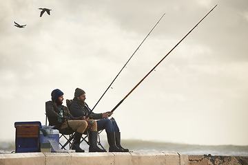 Image showing Sea, pole for fishing and men outdoor in winter, leisure activity at beach or harbor with friends in nature for seafood. Travel, ocean and waves with fisherman, recreation or hobby in the cold