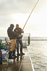 Image showing Fishing, men and net with fish at pier with rod, waves and relax on vacation, holiday and adventure. Friendship, people and bonding in morning with overcast, sky and nature for activity and hobby