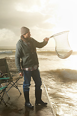 Image showing Sunshine, net and beach with man, fish and hobby with equipment, waves and weekend break. Person, ocean and guy with tools for activity and happiness with shore, pier and seaside with lens flare