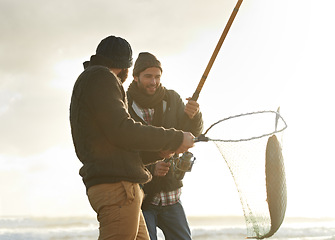 Image showing Fishing, men and net with fish at beach with rod, water and relax on vacation, holiday and travel. Friendship, people and bonding in morning with overcast, sky and nature for activity and hobby