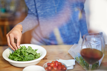 Image showing Person, cooking and prepare salad on table in kitchen closeup with wine in home for dinner. Tomato, lettuce and hands with healthy food in bowl to meal prep on counter for nutrition and diet in house