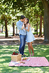 Image showing Couple, park and kiss in nature at picnic with love under the trees and enjoying romance in the summer sun. Cheerful, special and outdoor as partners and bonding with trust, care and commitment