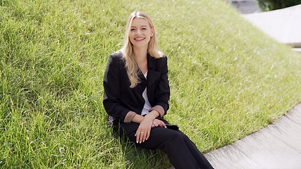 Image showing Smiling Woman in Black Suit Sitting on Green Grass