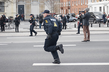 Image showing Police officer, man and running in street with crowd safety with protection service for public in city. People, law enforcement and justice in danger, arrest or warning on urban road in Copenhagen