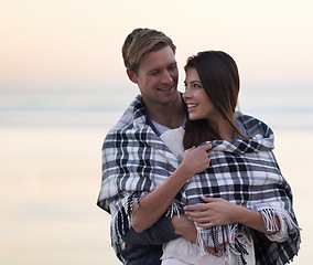 Image showing Couple, hug and sunset at beach with blanket for vacation, love and care in nature, outdoor and ocean. Man, woman and embrace with smile, bonding and happy for memory on holiday by sea in Australia