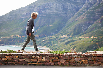 Image showing Travel, man and walking outdoor by mountain on holiday, vacation or trekking on trip in South Africa. Ocean, sea and person by stone wall for adventure, journey or tourist explore nature for hiking