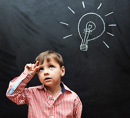 Image showing Kid, thinking and lightbulb on chalkboard for solution, learning and creative mindset in school with inspiration. Child, student or boy with light bulb on a blackboard for knowledge, vision or ideas