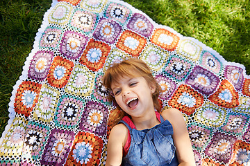 Image showing Laughing, top view and kid on blanket outdoor on grass in nature, smile and relax in summer. Funny, above and face of girl child on lawn with excited facial expression for comedy, joke and humor