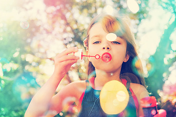 Image showing Portrait, nature and kid blowing bubbles at park, relax and girl having fun outdoor. Toy, garden and face of child with soap on summer vacation for recreation, leisure and playing game in low angle