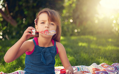 Image showing Park, portrait and child blowing bubbles on grass in nature, relax and kid having fun on blanket outdoor. Toy, garden and face of girl with soap on summer vacation for recreation, game or leisure