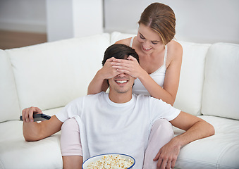 Image showing Couple, popcorn and covered eyes with sofa, surprise and remote for playful movie date. People, living room and film for relaxation, smile and bonding on couch with love and wow at home with break