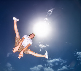 Image showing Boy, blue sky and jump outdoor with low angle, energy and lens flare of sunshine. Young teenager, below and leap in air by clouds in summer, moving and kid screaming for freedom with agile action