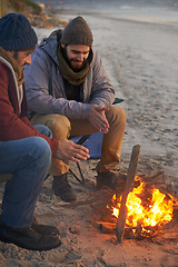 Image showing Men, sunset and campfire with cold hands, smile and happy from travel adventure and journey outdoor. Friends, ocean and sea with bonding, nature and vacation by a beach together on holiday with fire