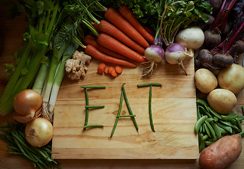 Image showing Vegetables, chopping board and kitchen with variety ingredients with the message eat. High angle, fresh from the earth and healthy green foods, herbs or organic produce harvest on wooden piece