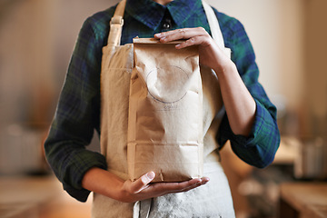 Image showing Barista woman, hands and bag while in an apron in background at home. Close up of female worker wearing pinafore and holding craft paper order while packaging coffee beans as small business owner