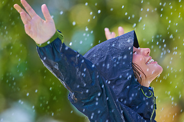 Image showing Woman, rain and freedom with a smile from winter climate, water and weather outdoor in a park. Happy, travel and female person with jacket for cold on holiday and vacation with raincoat and joy