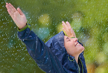 Image showing Woman, rain and freedom with a smile from wet climate, water and weather outdoor in a park. Happy, relax and female person with jacket for cold on holiday travel and vacation with raincoat and joy