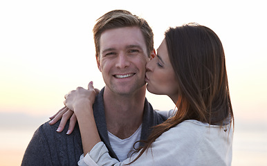 Image showing Love, kiss and couple on beach at sunset for tropical holiday adventure, relax and bonding together. Commitment, happy man and woman on romantic date with ocean, evening sky and embrace on vacation.