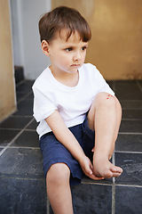 Image showing Little boy, sitting and injury on knee in home and accident, ache and with blood from cut. Young child, sad and holding hurt leg up with hand on foot, pain and sore on bruise with fear of trouble