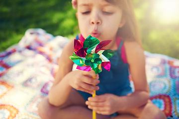Image showing Young girl, picnic and blowing pinwheel, garden and enjoying freedom of outside and happy. Colourful little child, backyard and summer for playing, toy and windmill for school holidays and happiness