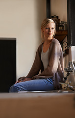 Image showing Portrait, young woman and sitting at home, looking out the window relaxing. Face, smile and happy calm female person, chilling and peaceful on her kitchen counter in a house while positive on weekend