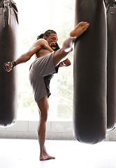 Image showing Man, kick boxing and bag with exercise, foot and combat for training with balance, power and precision in gym. African athlete, person or fighter with workout, fitness or strike for challenge in dojo
