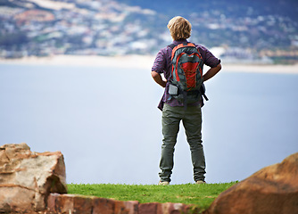 Image showing Person, hiking and back on mountains for fitness, outdoor and wellness in nature with cityscape in Europe. A hiker with backpack for trekking, journey and adventure or travel on a hill by an ocean