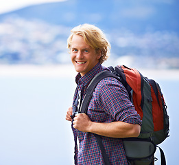 Image showing Man, trekking and portrait on mountains for travel, adventure and wellness by ocean, sea and vacation in Europe. Face of an excited, young person with backpack for hiking, explore and outdoor journey