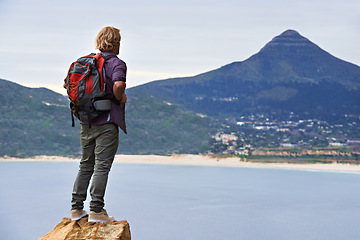 Image showing Man, backpack and hiking on mountain by ocean for travel, sightseeing or outdoor journey in nature. Rear view of male person, hiker or tourist with bag on rock for trekking, fitness or adventure