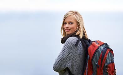 Image showing Woman, hiking and portrait for travel, adventure and wellness on a cloudy sky or grey background in winter. Face of a young person in backpack for trekking, explore or journey outdoor with mockup