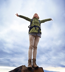 Image showing Woman, hiking and freedom on mountain top for travel, success and achievement or fresh air on cloudy sky. Young person in backpack and stretching arms for trekking, journey or adventure in low angle