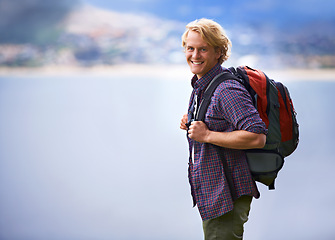 Image showing Man, hiking and portrait in nature for travel, adventure and wellness by ocean, sea and vacation in Europe. Face of an happy and young person with backpack for trekking, explore and outdoor journey