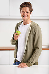 Image showing Smile, portrait and man with apple in kitchen of home for diet, health and wellness. Happy, confident and young male person eating fruit for organic, fresh and nutrition snack in modern apartment.