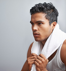 Image showing Face, fitness and towel with man breathing in studio isolated on gray background for workout. Exercise, sweating and intensity with confident young athlete on break from training for performance