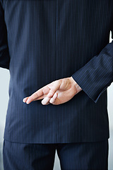 Image showing Businessman, back and fingers crossed with luck for hope, confidential or secret on a studio background. Closeup or rear view of man or business employee hiding hand in conspiracy, lie or corruption