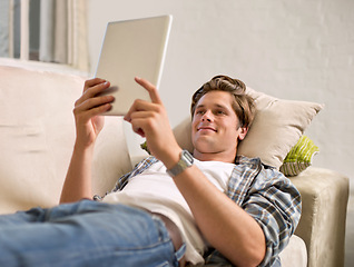 Image showing Tablet, relax and man on sofa in home for social media, networking and browse website. Happy, smile and person lying on couch with digital tech for internet, connection and streaming in living room