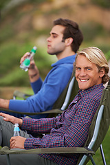 Image showing Camping, man and portrait with drinks for relax on grass in nature with happiness for holiday and vacation. People, smile and alcohol at campsite in woods for adventure, travel and bonding in forest