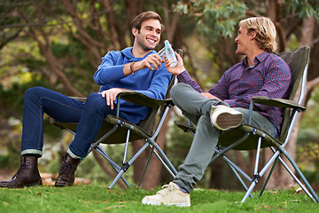 Image showing Camping, men and cheers with drinks for relax on grass in nature with happiness for holiday and vacation. People, smile and alcohol at campsite in woods for adventure, travel and bonding in forest