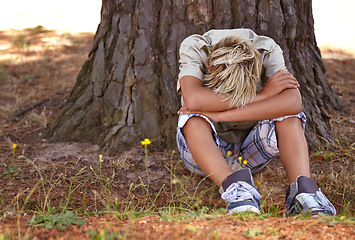 Image showing Sad boy, stress and depression by tree with anxiety, mental health or bored on grass in nature. Male person, child or teenager resting head on arms by stump in loneliness, childhood or left out