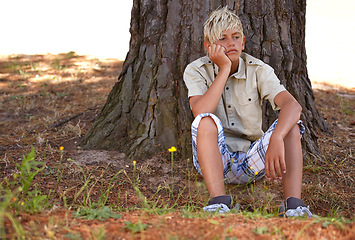 Image showing Boy, bored and depression by tree with anxiety, mental health or stress on grass in nature. Young male person, child or teenager resting on break by wood stump in loneliness, childhood or left out