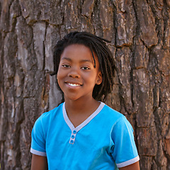 Image showing Happy portrait, black child and tree in fashion, hairstyle or childhood for outdoor nature. Face of young African, male person or teenager with smile, blue tshirt or casual clothing by bark or forest