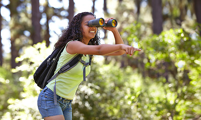 Image showing Happy girl, binoculars and pointing in nature with backpack for sightseeing, explore or outdoor vision. Young female person, child or teenager enjoying adventure, bird watching or search in forest