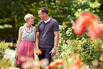 Image showing Love, holding hands and couple in a park with care, support and trust while bonding outdoor. Security, travel and people walking in a field of flowers for holiday, vacation or romantic summer date